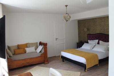 Jardin verdoyant avec un ruisseau traversant, entouré de grandes feuilles et d'arbustes fleuris, près d'une maison en pierre.