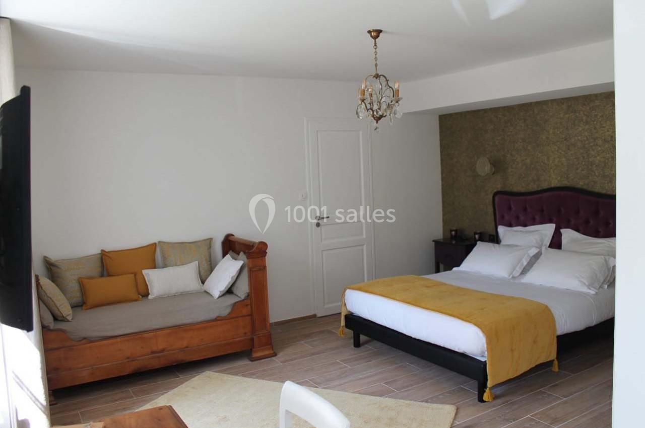 Chambre lumineuse avec un lit double, un canapé en bois, un lustre et des murs blancs, décorée dans des tons chauds.