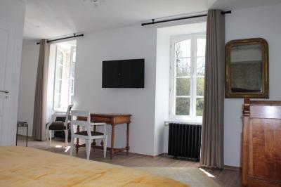 Jardin verdoyant avec un ruisseau traversant, entouré de grandes feuilles et d'arbustes fleuris, près d'une maison en pierre.