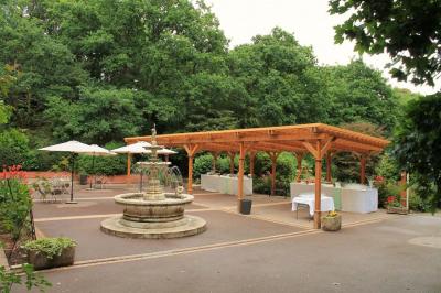 Jardin verdoyant avec un ruisseau traversant, entouré de grandes feuilles et d'arbustes fleuris, près d'une maison en pierre.