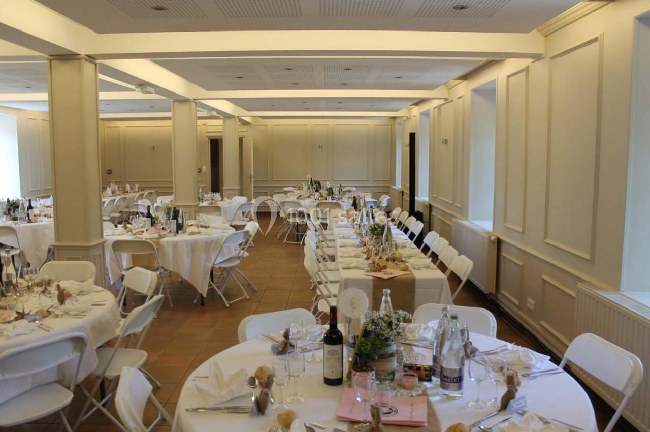 Salle de réception lumineuse avec des tables rondes dressées pour un événement, décorées de bouteilles et de centres de…