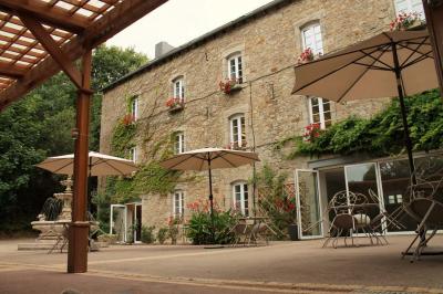 Jardin verdoyant avec un ruisseau traversant, entouré de grandes feuilles et d'arbustes fleuris, près d'une maison en pierre.
