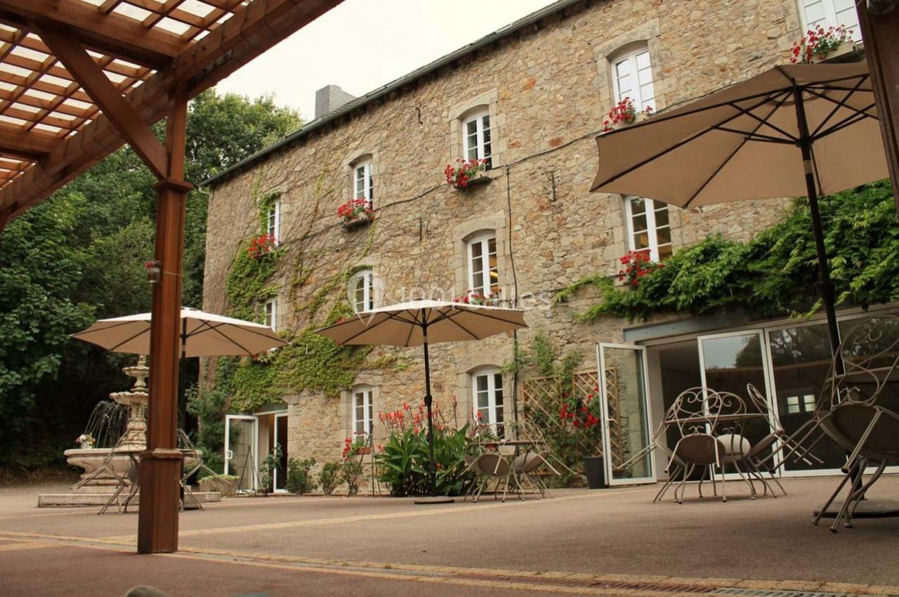 Cour intérieure avec fontaine, parasols, tables et chaises en fer forgé devant un bâtiment en pierre avec fenêtres fleuries.