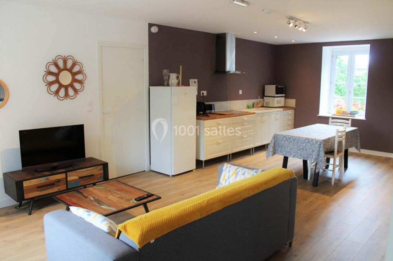 Salon avec canapé, table à manger, cuisine équipée et fenêtre donnant sur un extérieur verdoyant.