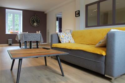 Jardin verdoyant avec un ruisseau traversant, entouré de grandes feuilles et d'arbustes fleuris, près d'une maison en pierre.