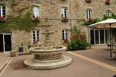 Jardin verdoyant avec un ruisseau traversant, entouré de grandes feuilles et d'arbustes fleuris, près d'une maison en pierre.