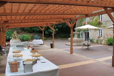 Jardin verdoyant avec un ruisseau traversant, entouré de grandes feuilles et d'arbustes fleuris, près d'une maison en pierre.