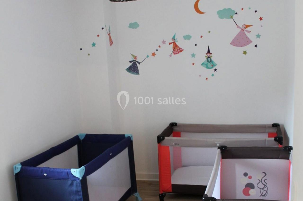 Deux lits parapluie dans une chambre décorée avec des stickers de fées, étoiles et lune sur un mur blanc.