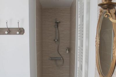 Jardin verdoyant avec un ruisseau traversant, entouré de grandes feuilles et d'arbustes fleuris, près d'une maison en pierre.