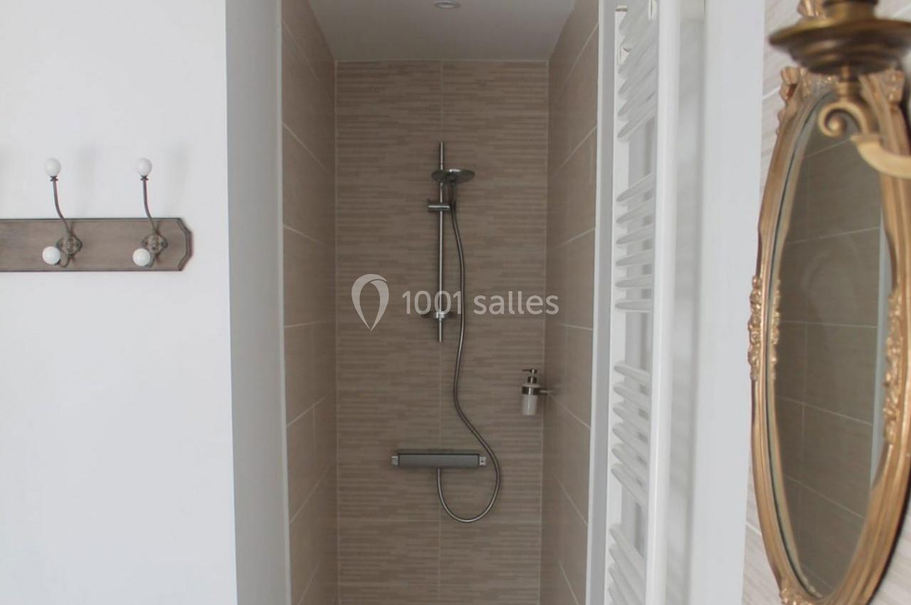 Douche moderne avec carrelage beige, pommeau mural et porte-savon, située dans une salle de bain lumineuse.