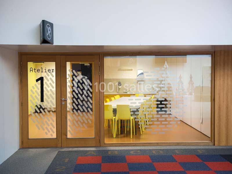 Salle de réunion moderne avec une grande table blanche, chaises jaunes et vitres décorées de motifs géométriques.