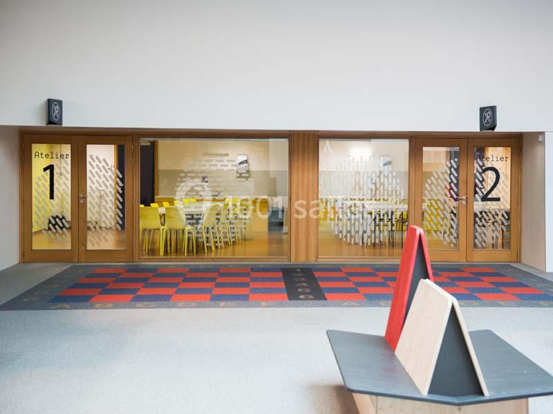 Vue sur deux salles d'atelier vitrées, numérotées 1 et 2, avec des tables et chaises jaunes à l'intérieur.