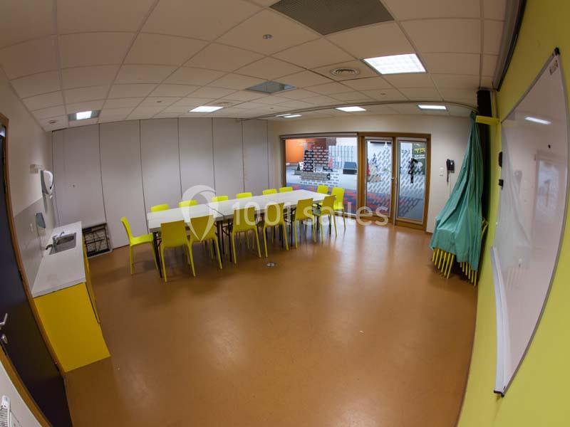 Salle de réunion lumineuse avec une grande table, des chaises jaunes, un tableau blanc et des baies vitrées.