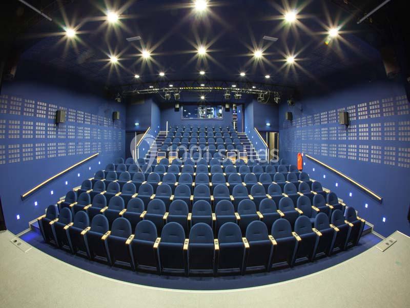 Salle de cinéma vide avec des rangées de sièges bleus et un éclairage au plafond.