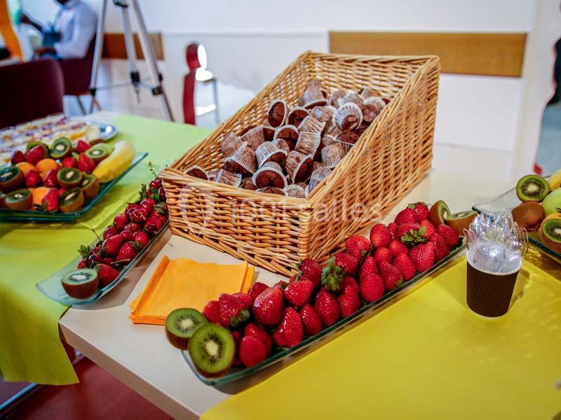 Plateau de fruits frais avec fraises, kiwis et bananes, accompagné de muffins dans un panier en osier sur une table.