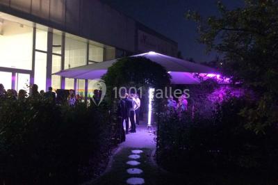 Un groupe de personnes rassemblé sous un grand parasol éclairé par des lumières violettes, dans un jardin de nuit.