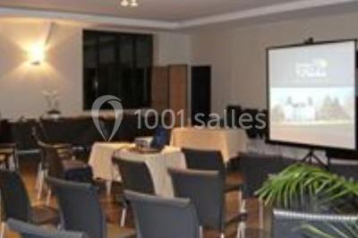 Salle de réunion avec des chaises disposées face à un écran de projection allumé, éclairage tamisé.