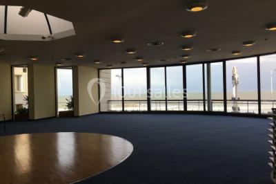 Vue intérieure d'une salle circulaire avec de grandes baies vitrées donnant sur la mer et un ciel partiellement nuageux.
