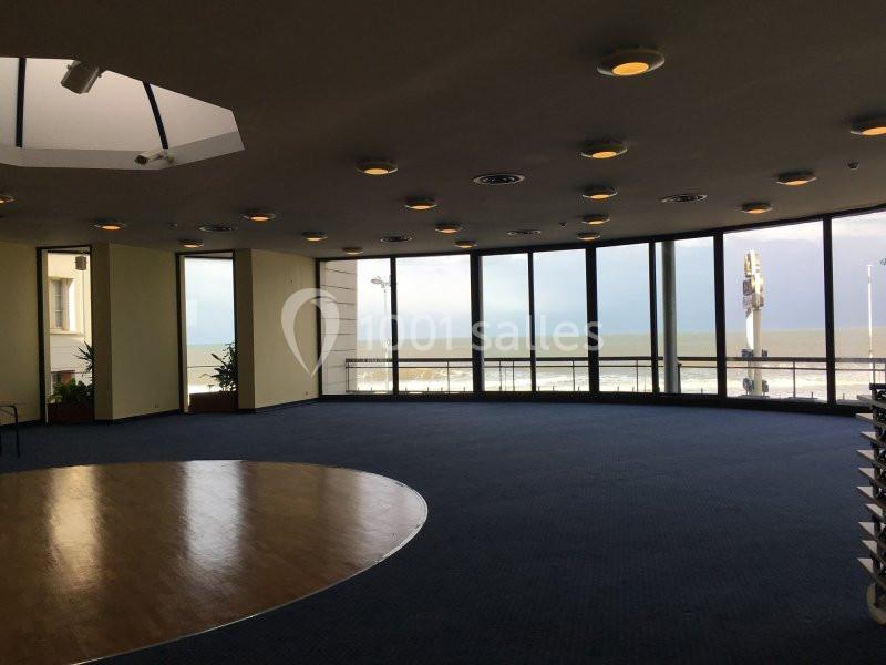 Salle circulaire avec de grandes baies vitrées offrant une vue sur la mer et un sol en moquette bleue.