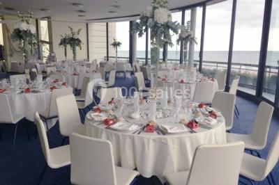 Vue intérieure d'une salle circulaire avec de grandes baies vitrées donnant sur la mer et un ciel partiellement nuageux.