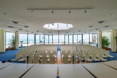 Vue intérieure d'une salle circulaire avec de grandes baies vitrées donnant sur la mer et un ciel partiellement nuageux.
