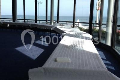 Miniature Location salle Villers-sur-Mer (Calvados) - Salle Panoramique Villers Sur Mer #5 Salle avec de grandes baies vitrées, tables dressées avec nappes orange, assiettes bleues et verres, vue sur un bâtiment…