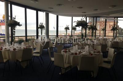 Miniature Location salle Villers-sur-Mer (Calvados) - Salle Panoramique Villers Sur Mer #12 Salle avec de grandes baies vitrées, tables dressées avec nappes orange, assiettes bleues et verres, vue sur un bâtiment…