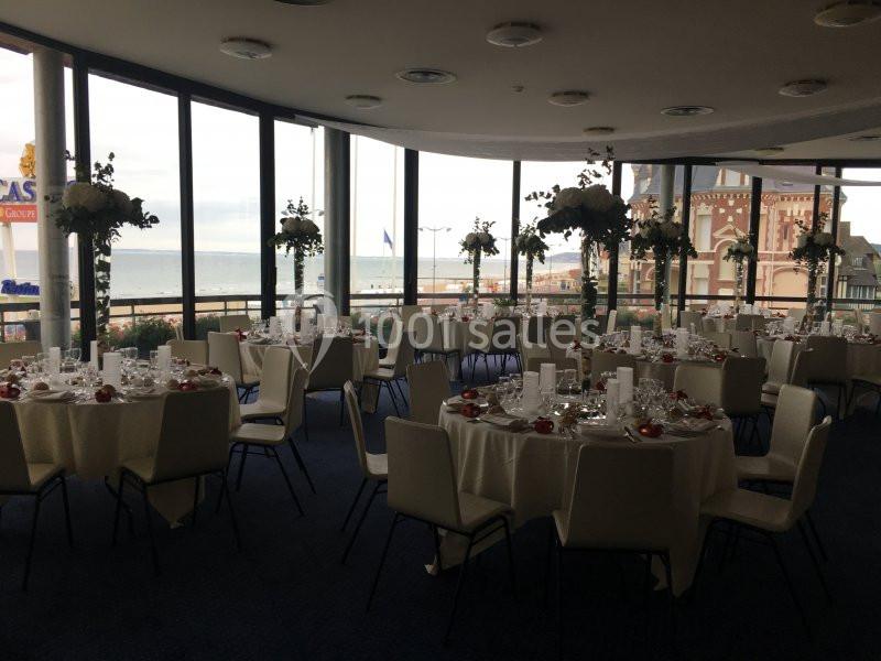 Location salle Villers-sur-Mer (Calvados) - Salle Panoramique Villers Sur Mer #12 Salle de réception élégante avec tables rondes dressées, grandes baies vitrées offrant une vue sur la mer et des bâtiments.