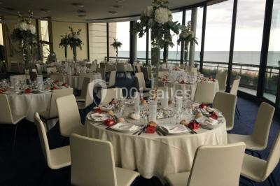 Miniature Location salle Villers-sur-Mer (Calvados) - Salle Panoramique Villers Sur Mer #13 Salle avec de grandes baies vitrées, tables dressées avec nappes orange, assiettes bleues et verres, vue sur un bâtiment…