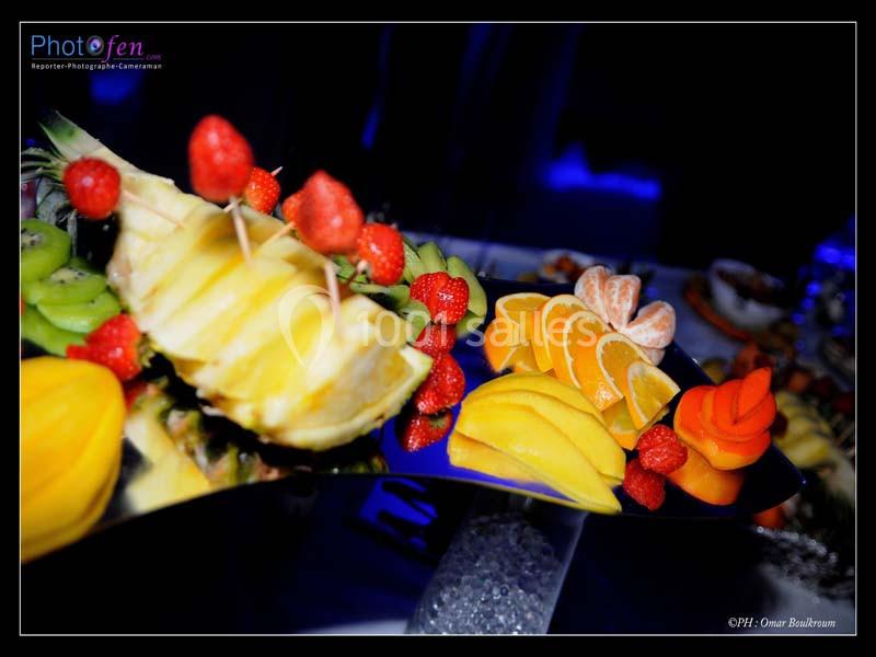 Plateau de fruits variés avec ananas, fraises, kiwis, mangues et agrumes, présenté sur un miroir.