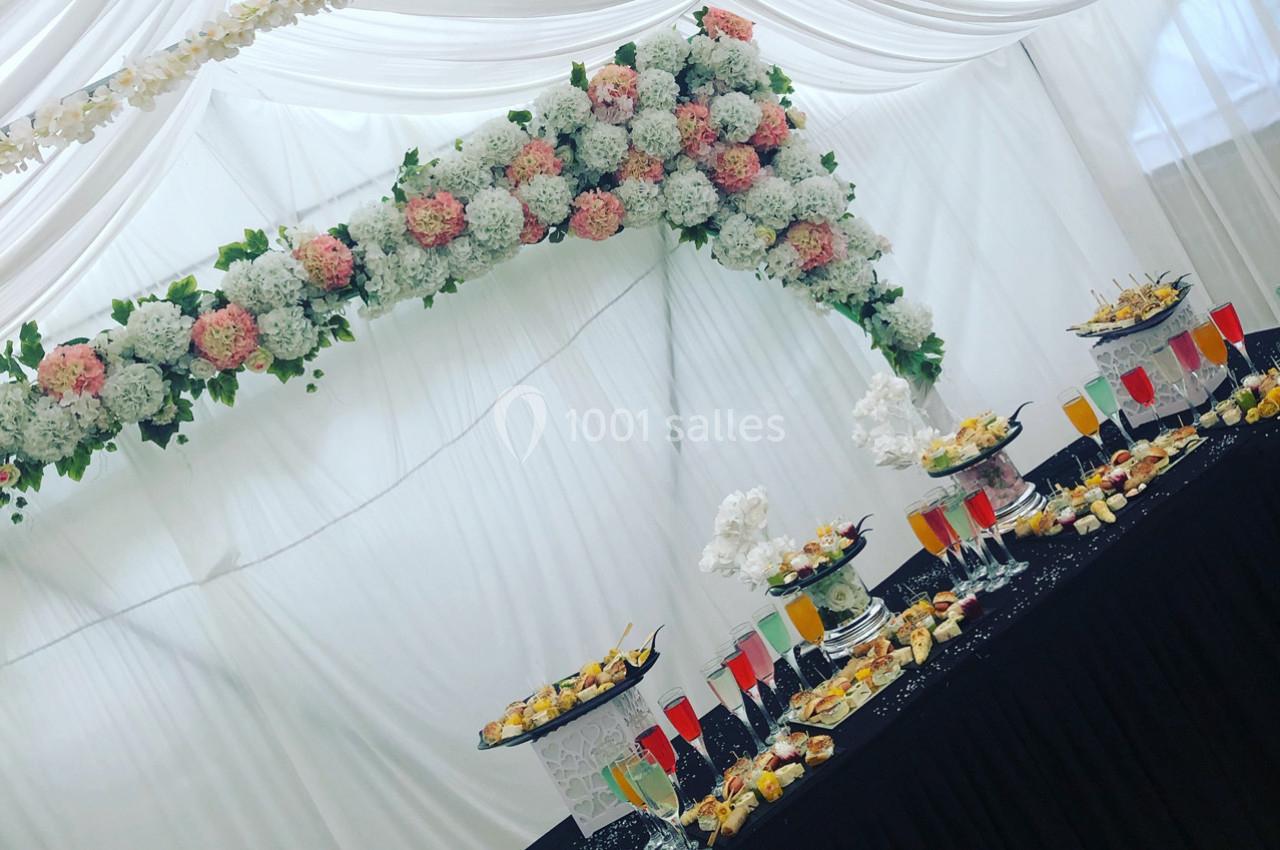 Table de buffet décorée avec des fleurs blanches et roses suspendues, sous un drapé blanc élégant.