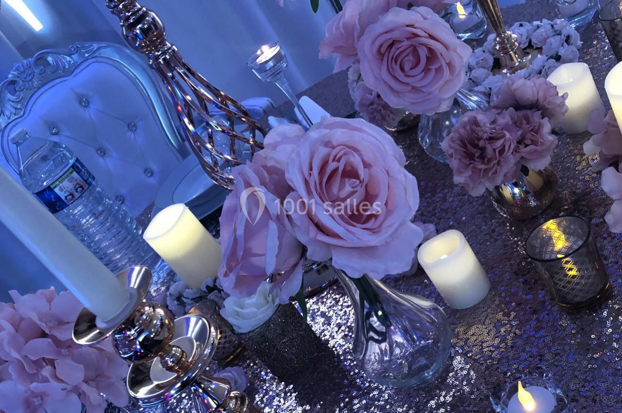 Décoration de table élégante avec roses roses, bougies allumées et accessoires dorés sur une nappe scintillante.