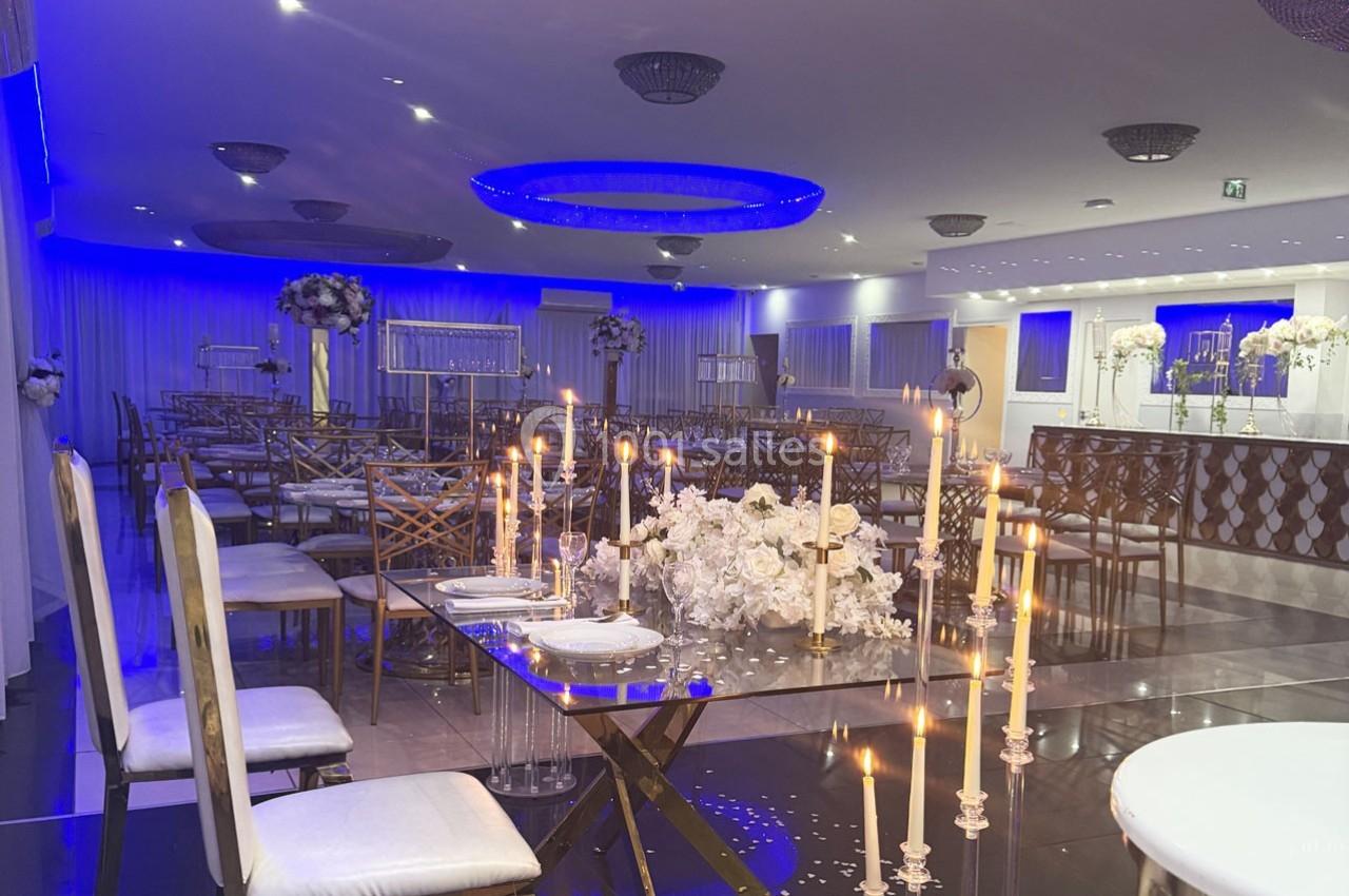 Salle de réception élégante avec tables décorées de bougies et fleurs blanches, éclairage bleu tamisé.