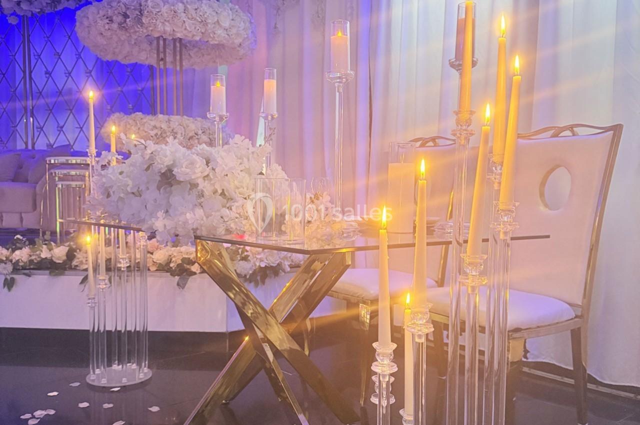 Bougies allumées sur des chandeliers en verre entourant une table et des chaises dans une décoration élégante et lumineuse.