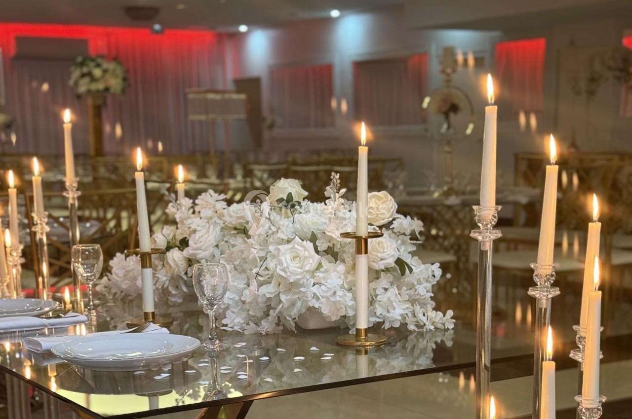 Table décorée avec des chandeliers allumés, des fleurs blanches et de la vaisselle, dans une salle élégamment éclairée.