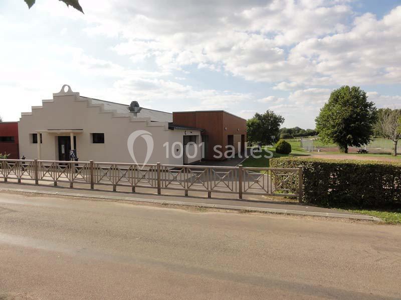 Bâtiment moderne avec façade blanche et brune, entouré d'espaces verts, vu depuis une route bordée d'une barrière.