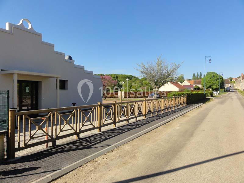 Façade d'un bâtiment moderne avec une rampe d'accès en bois, bordée d'une rue calme et de maisons résidentielles.