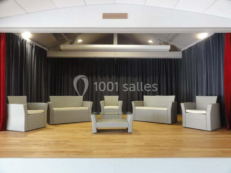 Mobilier en rotin clair composé de fauteuils, canapés et table basse, disposé sur une scène en bois avec rideaux sombres.