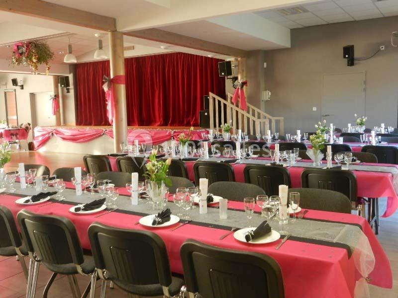 Salle décorée pour un événement avec tables dressées en rose et noir, et une scène avec rideaux rouges en arrière-plan.