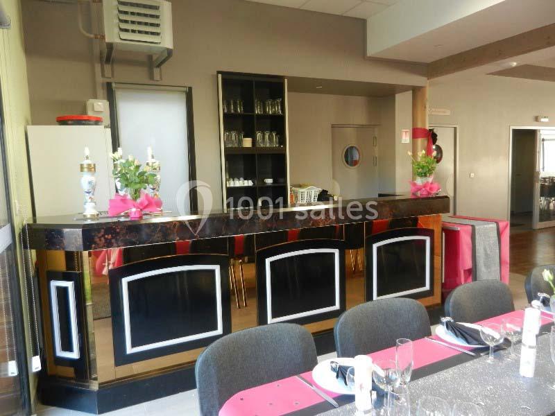 Comptoir de bar noir et blanc avec décorations florales, situé dans une salle aménagée avec tables dressées.