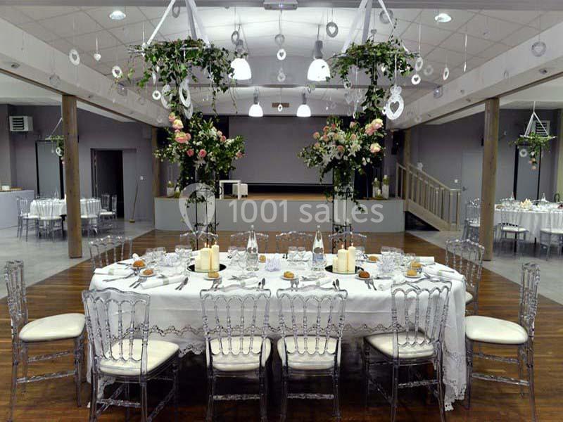 Salle de réception décorée avec des tables élégantes, des chaises transparentes et des arrangements floraux suspendus.