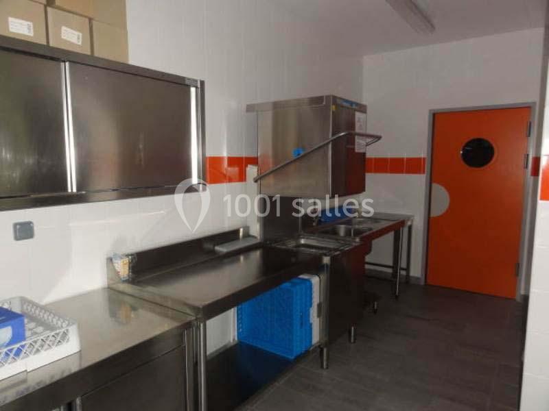 Cuisine professionnelle avec plans de travail en inox, lave-vaisselle industriel et porte orange au fond.