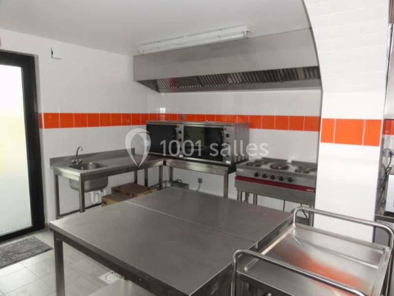 Cuisine professionnelle équipée avec plans de travail en inox, fours, plaques de cuisson et évier.