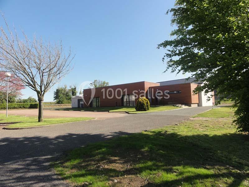 Bâtiment moderne de plain-pied avec façade en bois, entouré d'arbres et d'une allée asphaltée sous un ciel dégagé.