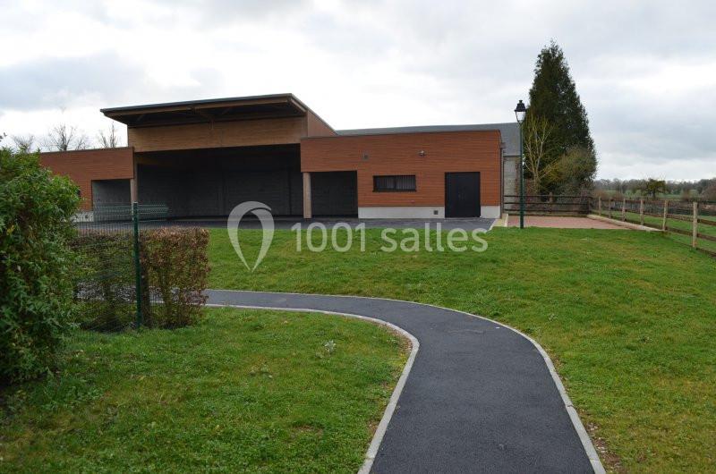 Bâtiment moderne en bois avec une allée asphaltée sinueuse, entouré de pelouse et de végétation.
