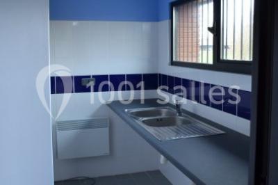 Cuisine avec un évier en inox, un plan de travail sombre, un réfrigérateur blanc et des murs bleus.