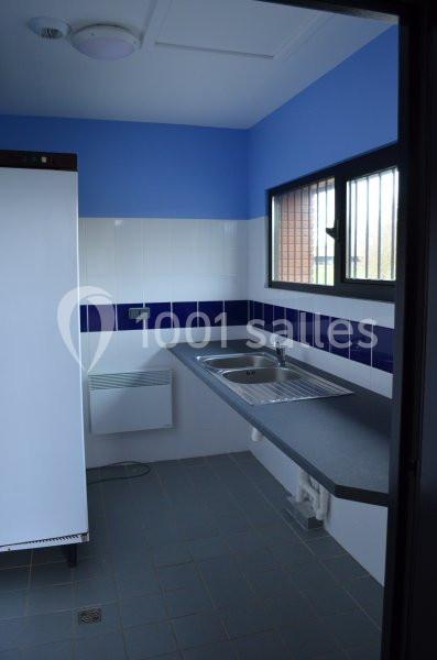 Cuisine avec un évier en inox, un plan de travail sombre, un réfrigérateur blanc et des murs bleus.