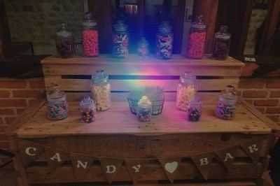 Buffet en bois décoré avec des bocaux de bonbons colorés et une guirlande ’Candy Bar’ dans un cadre rustique.