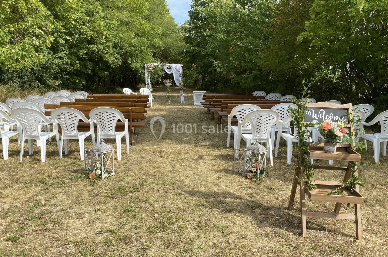 Allée centrale bordée de chaises blanches et bancs en bois menant à une arche de mariage décorée dans un cadre extérieur…