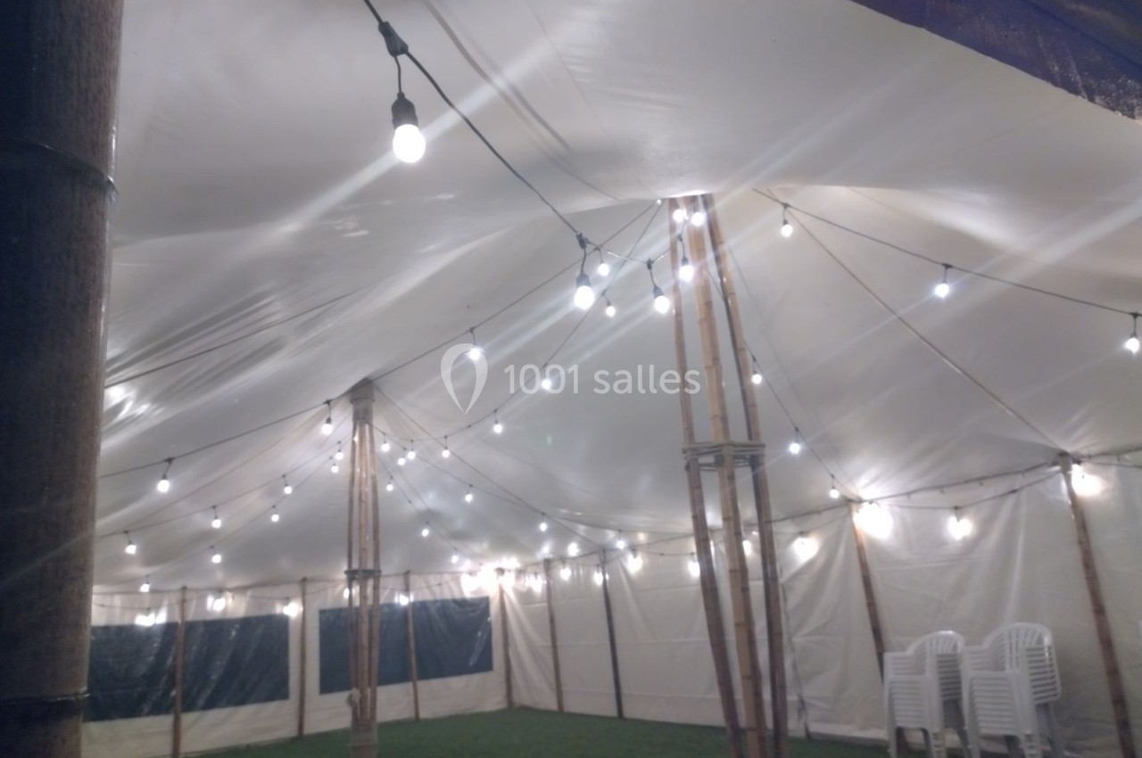 Intérieur d'une tente éclairée par des guirlandes lumineuses suspendues, avec des chaises empilées dans un coin.